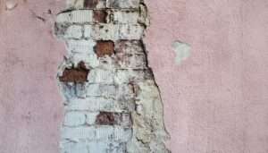 Close-up of peeling paint on an HDB wall, indicating moisture damage. HDB painting services